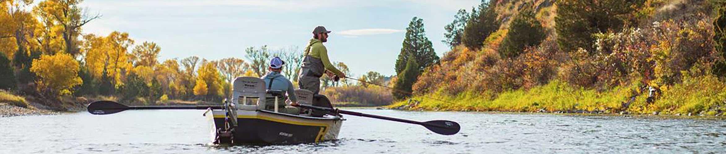 An angler fly fishing from a boat on a river lined with fall colors. 