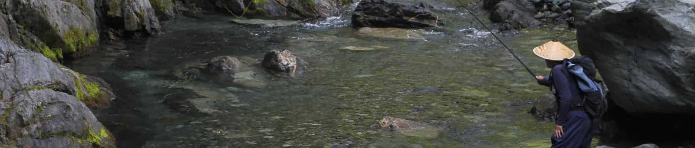 An angler stalking fish using a Tenkara rod in a crystal-clear backcountry creek