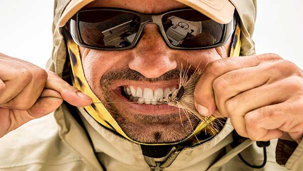 A guide tying on a fly and cinching down the knot with his teeth wile fishing for golden dorado in Argentina